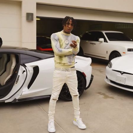Armani Gaulden's father, Kentrell DeSean Gaulden posing infront of his cars. He is wearing white pants, miced colored t-shirtand white shoes